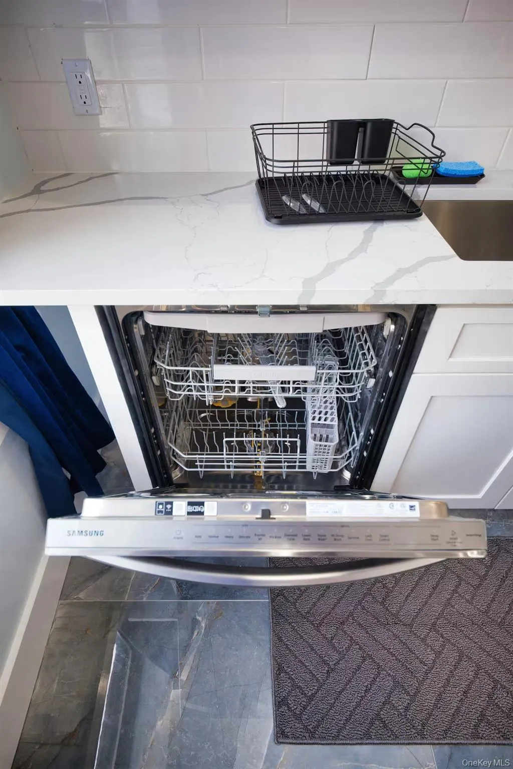 Kitchen view of dishwashing machine, tasteful backsplash, light stone countertops, and white cabinets Kitchen view of dishwashing machine, tasteful backsplash, light stone countertops, and white cabinets