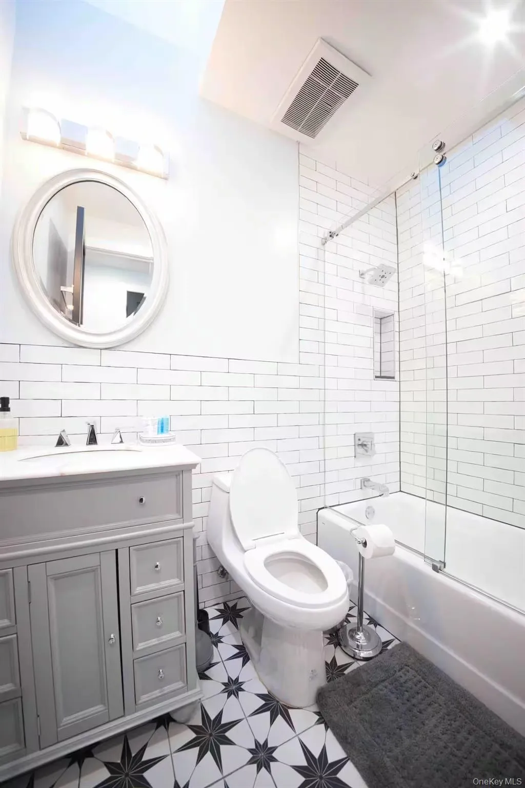 Full bath featuring light floors, vanity, shower / bath combination with glass door, and tile walls Full bath featuring light floors, vanity, shower / bath combination with glass door, and tile walls