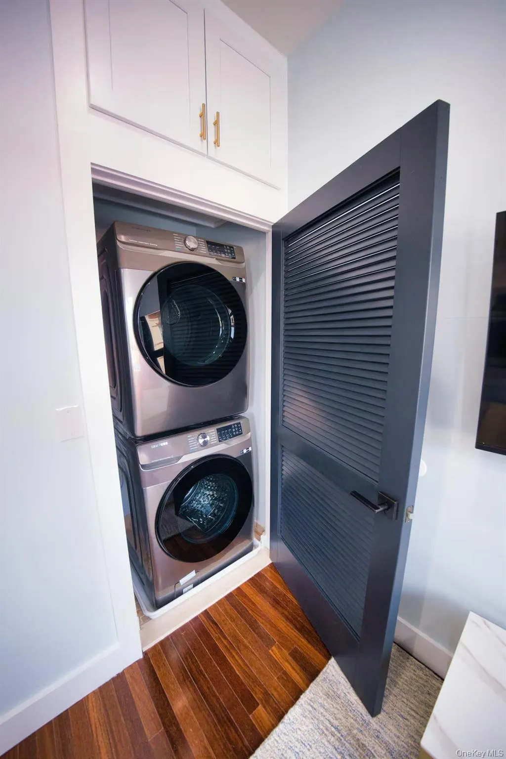 Washroom with stacked washer / dryer and dark wood finished floors Washroom with stacked washer / dryer and dark wood finished floors