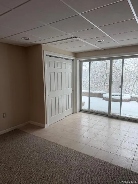 Unfurnished bedroom with a drop ceiling, a closet, access to outside, light colored carpet, and light tile patterned floors Unfurnished bedroom with a drop ceiling, a closet, access to outside, light colored carpet, and light tile patterned floors