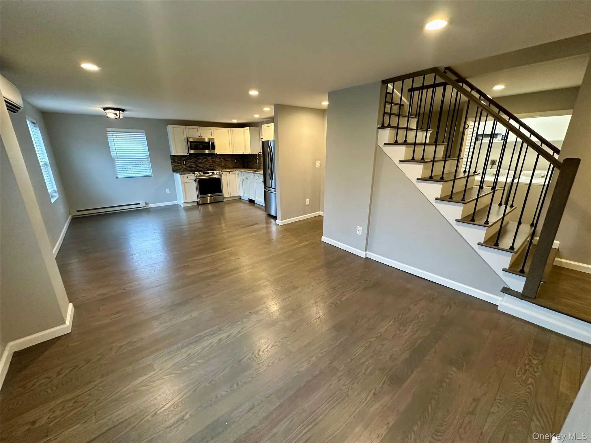 Unfurnished living room featuring stairs, dark wood-style flooring, recessed lighting, and a baseboard heating unit Unfurnished living room featuring stairs, dark wood-style flooring, recessed lighting, and a baseboard heating unit
