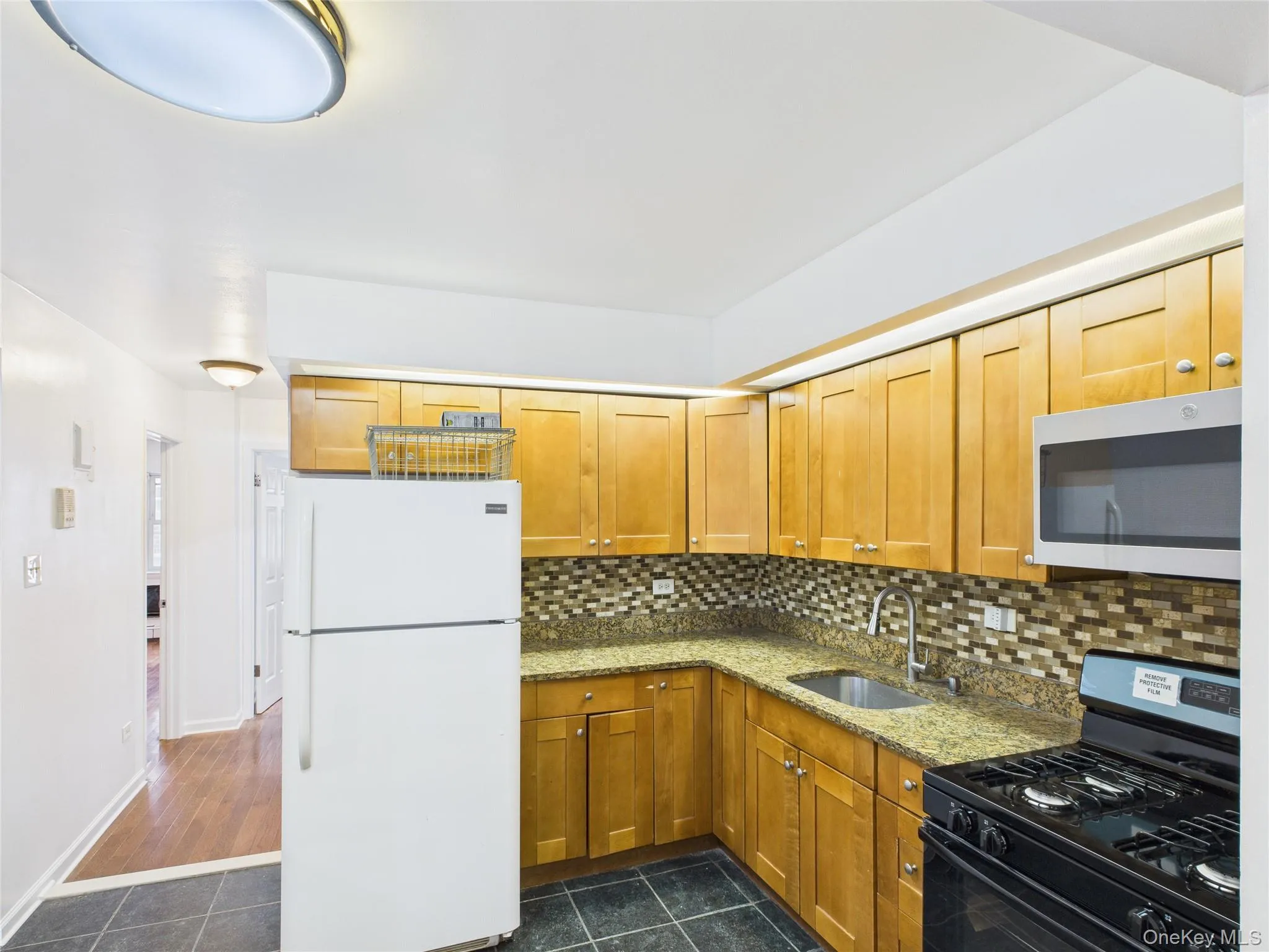 Kitchen with black range with gas stovetop, freestanding refrigerator, light stone countertops, dark tile patterned flooring, and decorative backsplash Kitchen with black range with gas stovetop, freestanding refrigerator, light stone countertops, dark tile patterned flooring, and decorative backsplash