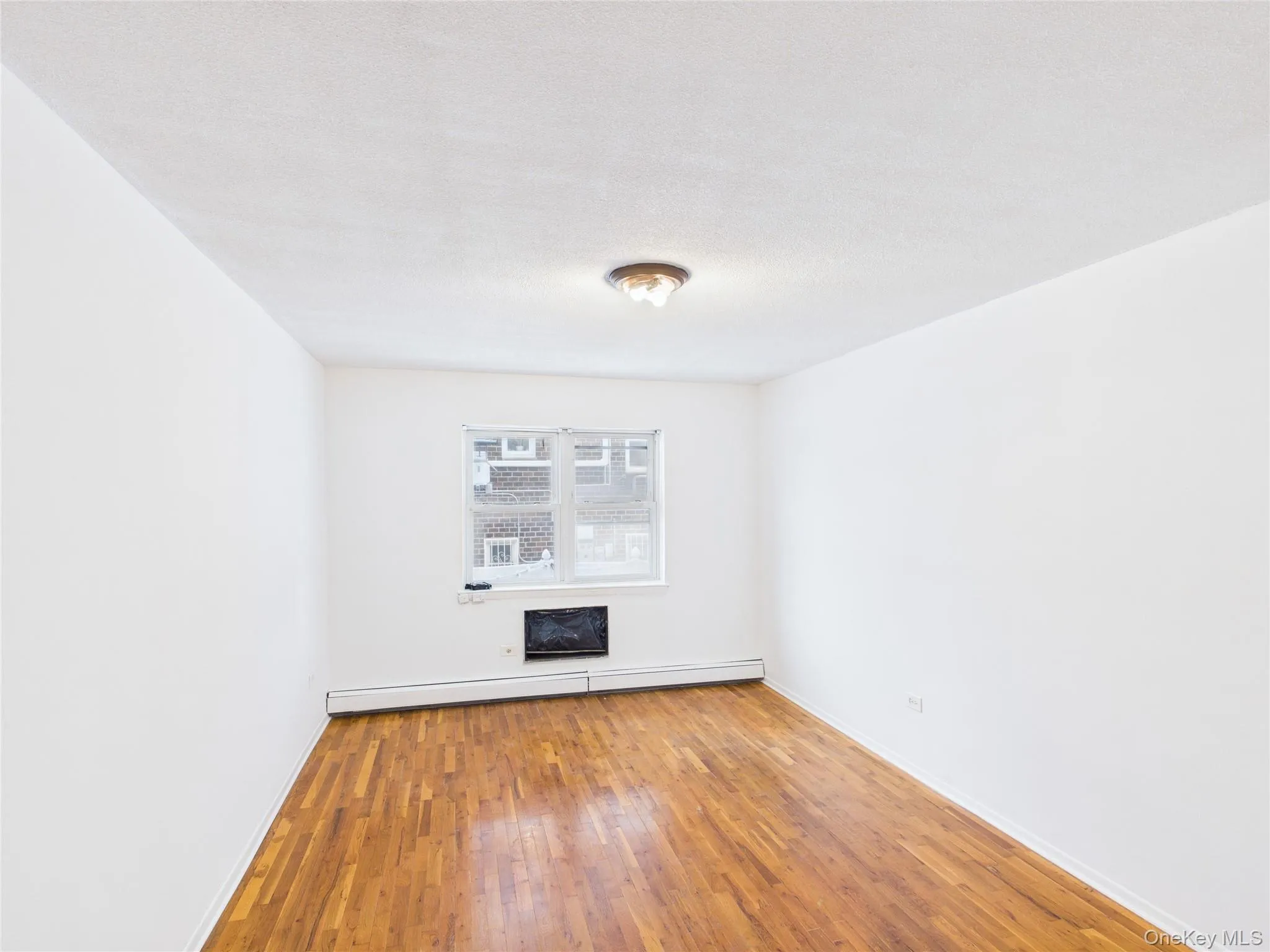 Unfurnished living room with a baseboard heating unit, wood-type flooring, and a textured ceiling Unfurnished living room with a baseboard heating unit, wood-type flooring, and a textured ceiling