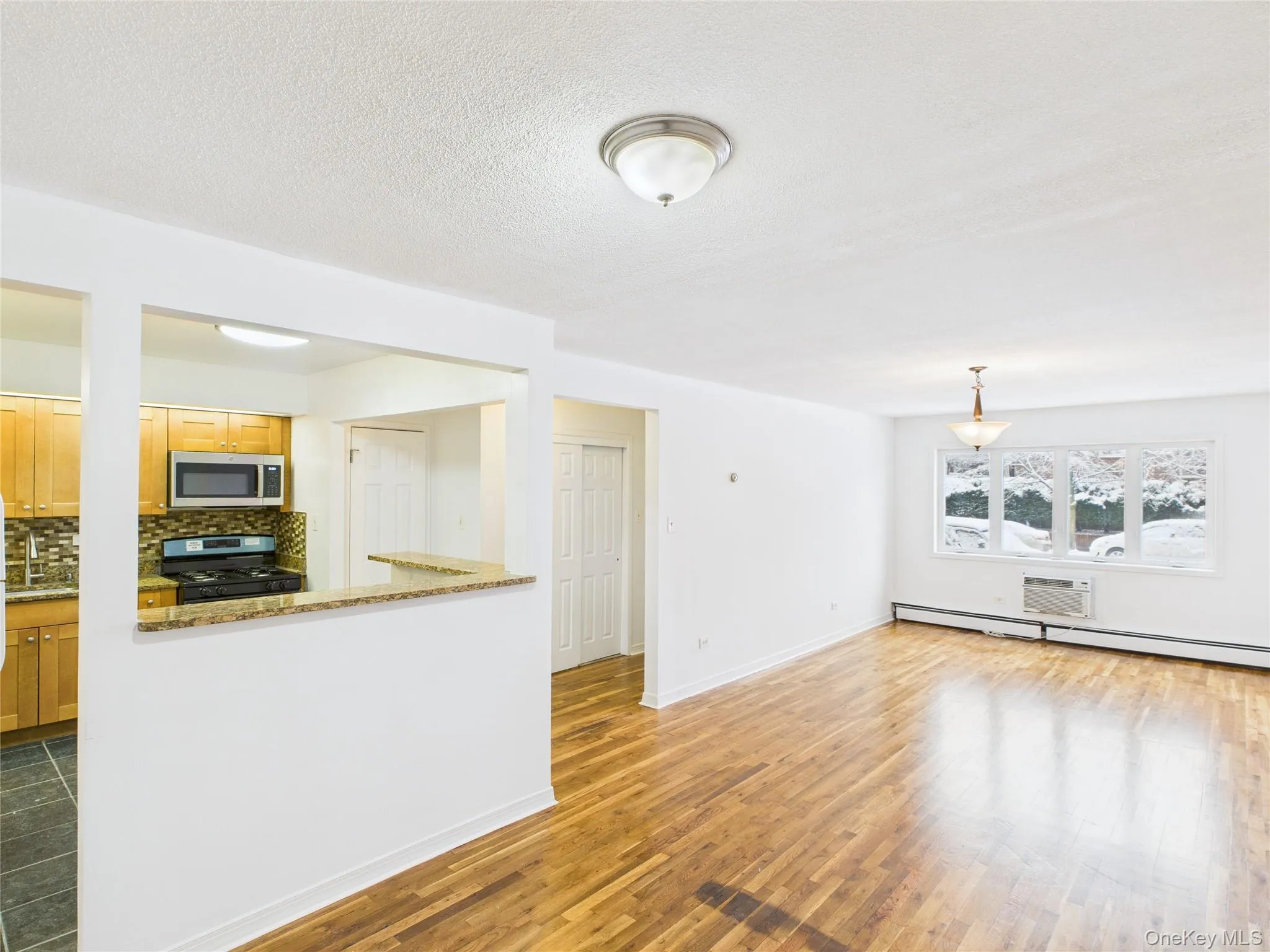 Unfurnished living room featuring light wood finished floors, a baseboard heating unit, a wall mounted AC, and a textured ceiling Unfurnished living room featuring light wood finished floors, a baseboard heating unit, a wall mounted AC, and a textured ceiling