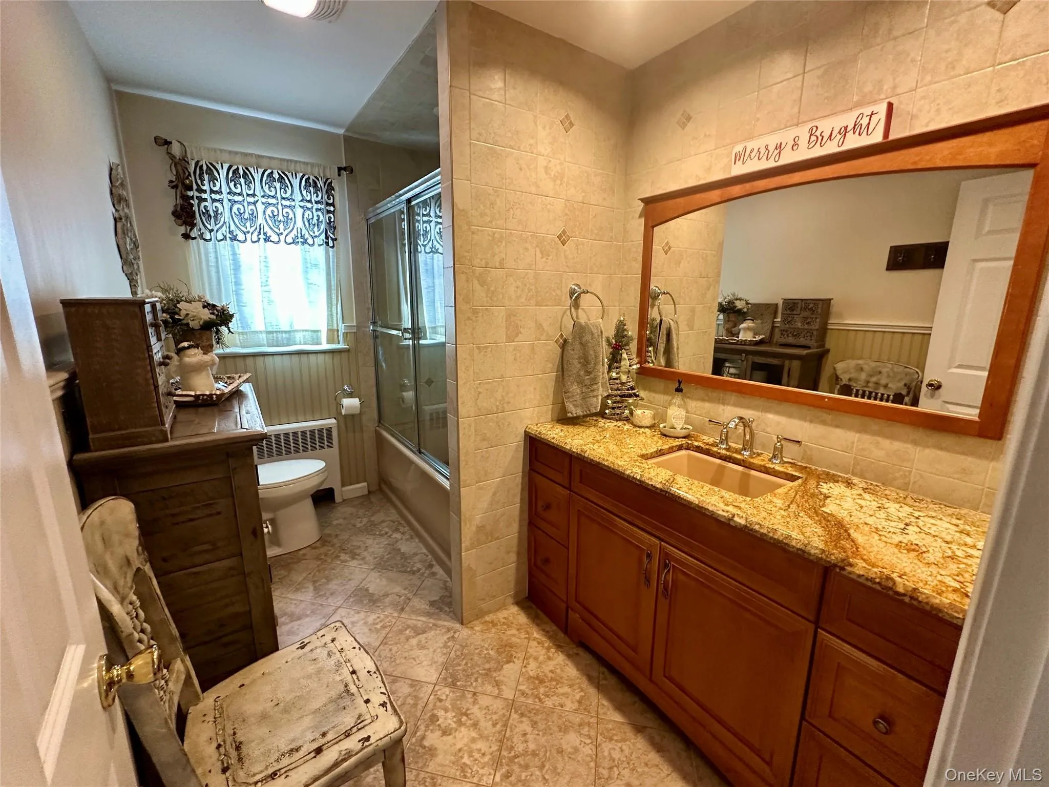 Bathroom with vanity, enclosed tub / shower combo, radiator heating unit, tile walls, and light tile patterned flooring Bathroom with vanity, enclosed tub / shower combo, radiator heating unit, tile walls, and light tile patterned flooring