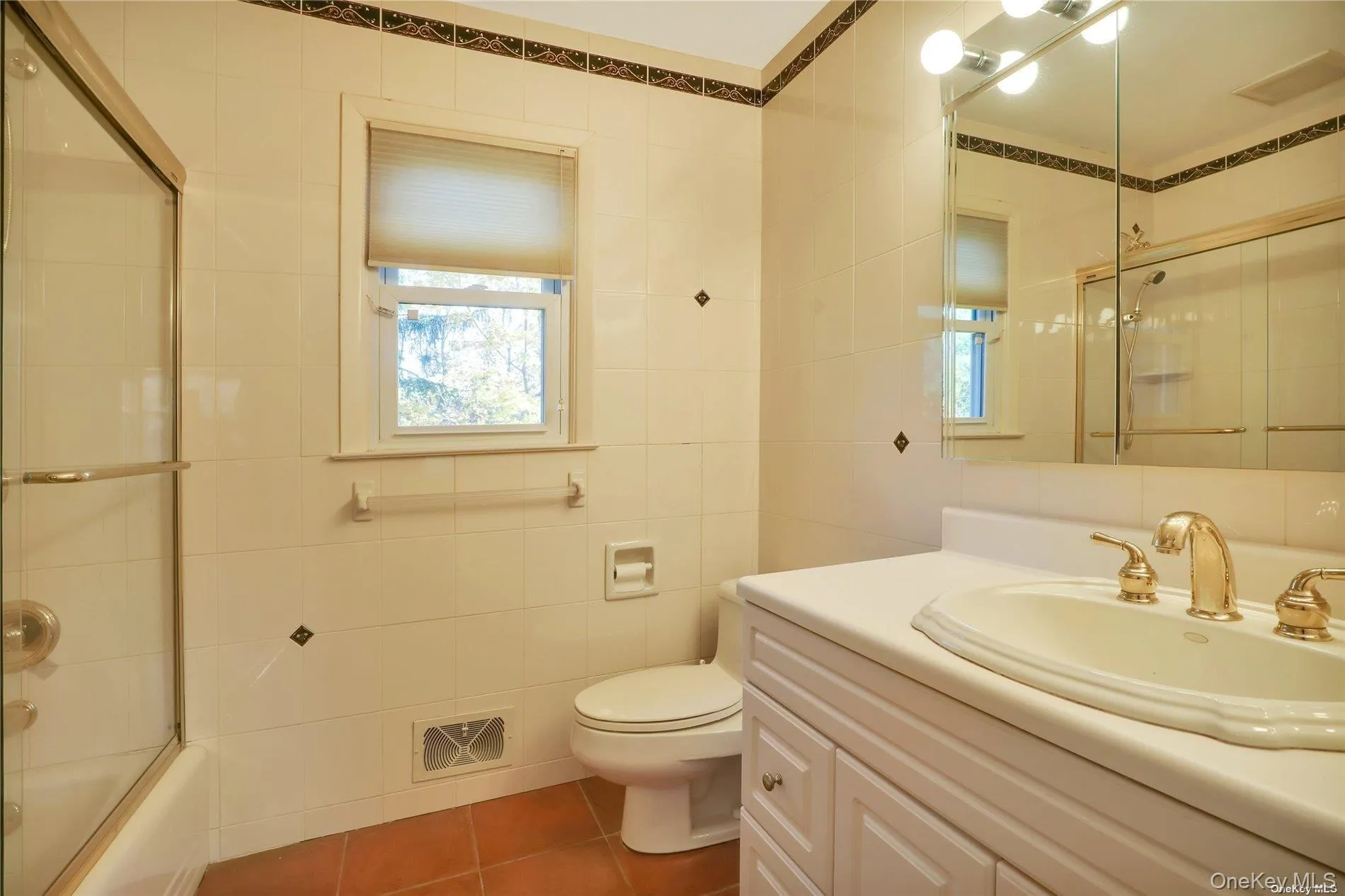 Full bath featuring vanity, tile patterned flooring, tile walls, and shower / bath combination with glass door Full bath featuring vanity, tile patterned flooring, tile walls, and shower / bath combination with glass door