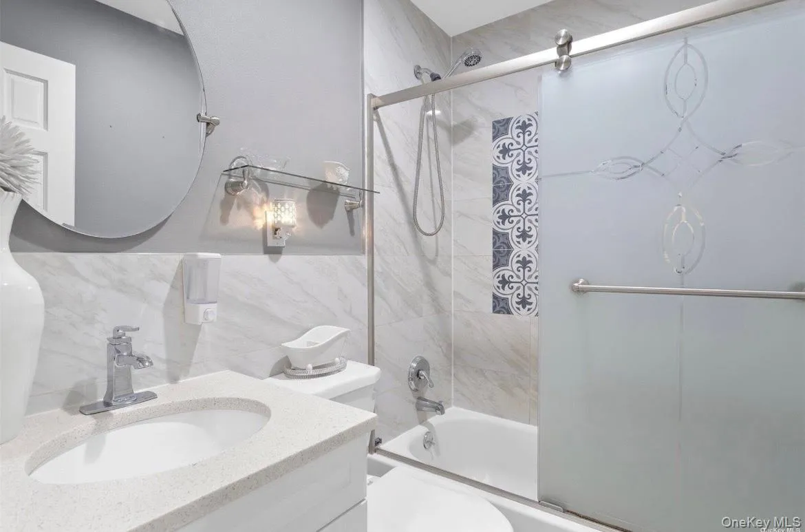 Bathroom featuring bath / shower combo with glass door, vanity, tile walls, and wainscoting Bathroom featuring bath / shower combo with glass door, vanity, tile walls, and wainscoting