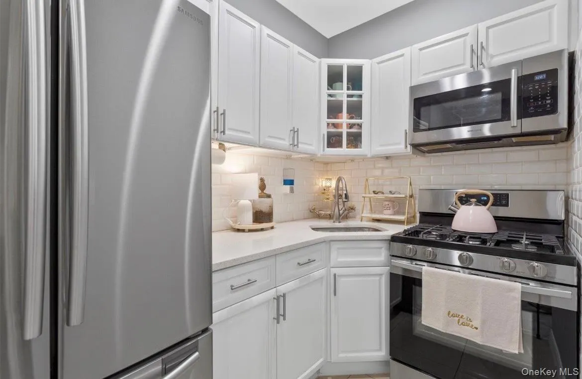 Kitchen featuring stainless steel appliances, white cabinetry, glass insert cabinets, and light stone countertops Kitchen featuring stainless steel appliances, white cabinetry, glass insert cabinets, and light stone countertops