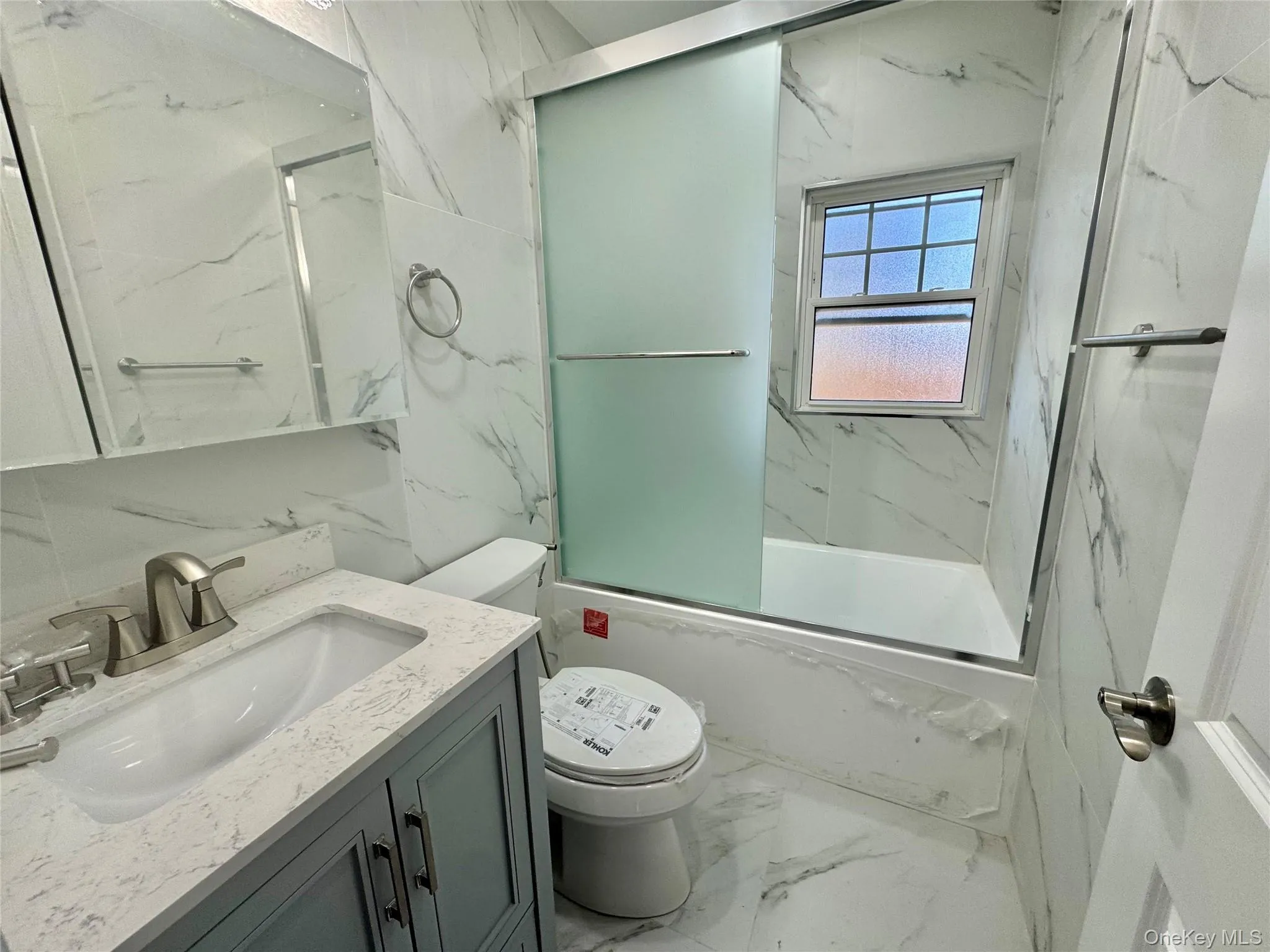 Full bath with marble tiled floors, vanity, bath / shower combo with glass door, stone wall, and tile walls Full bath with marble tiled floors, vanity, bath / shower combo with glass door, stone wall, and tile walls