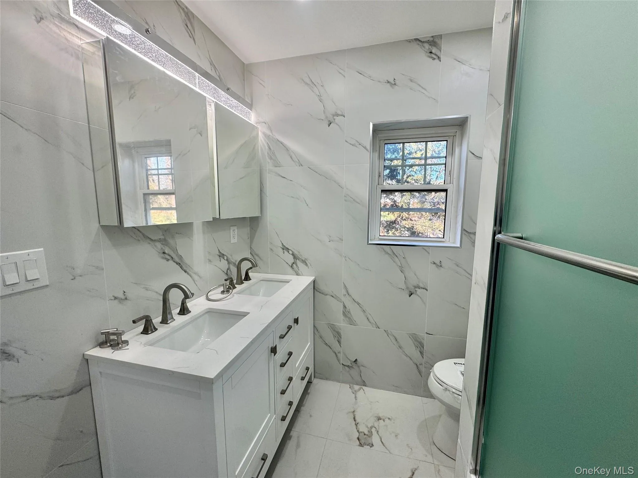 Full bath with double vanity, light marble finish flooring, and stone wall Full bath with double vanity, light marble finish flooring, and stone wall