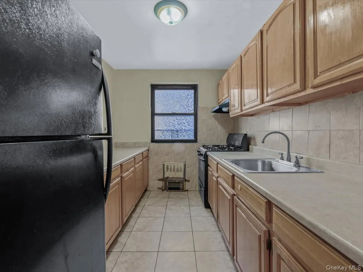 Kitchen featuring black appliances, light countertops, light tile patterned floors, and brown cabinetry Kitchen featuring black appliances, light countertops, light tile patterned floors, and brown cabinetry