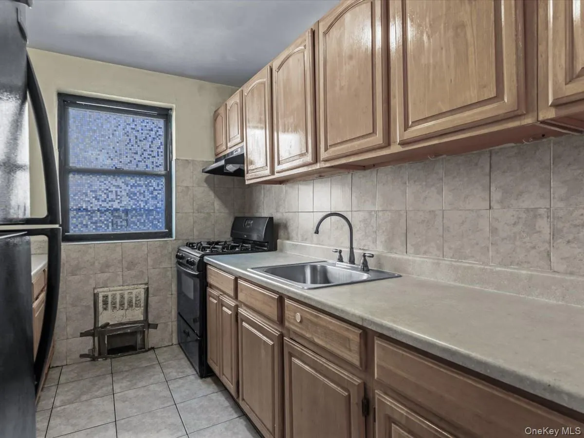 Kitchen featuring black appliances, light countertops, light tile patterned flooring, under cabinet range hood, and tile walls Kitchen featuring black appliances, light countertops, light tile patterned flooring, under cabinet range hood, and tile walls