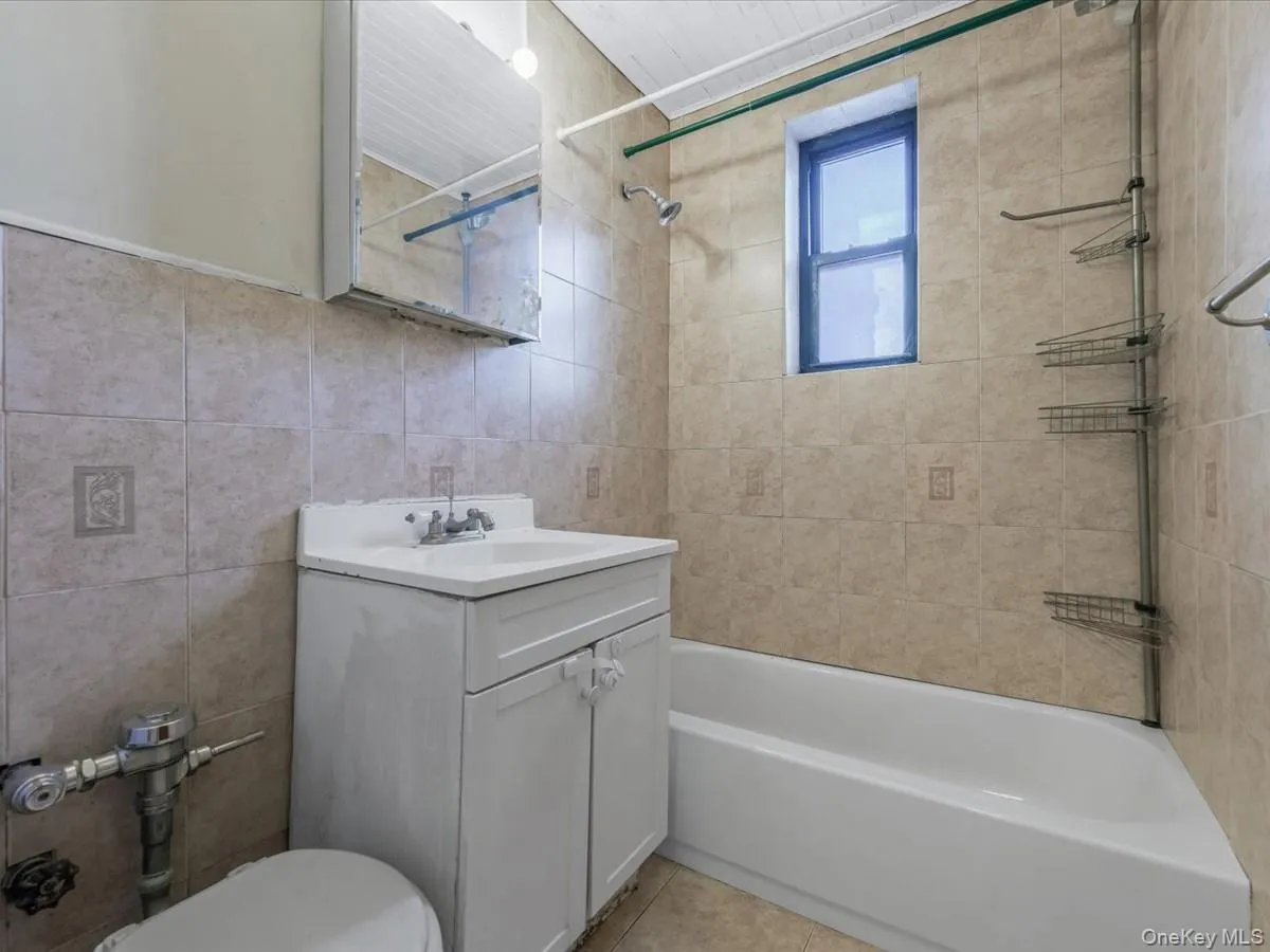 Bathroom with vanity, tile walls, tub / shower combination, and light tile patterned flooring Bathroom with vanity, tile walls, tub / shower combination, and light tile patterned flooring