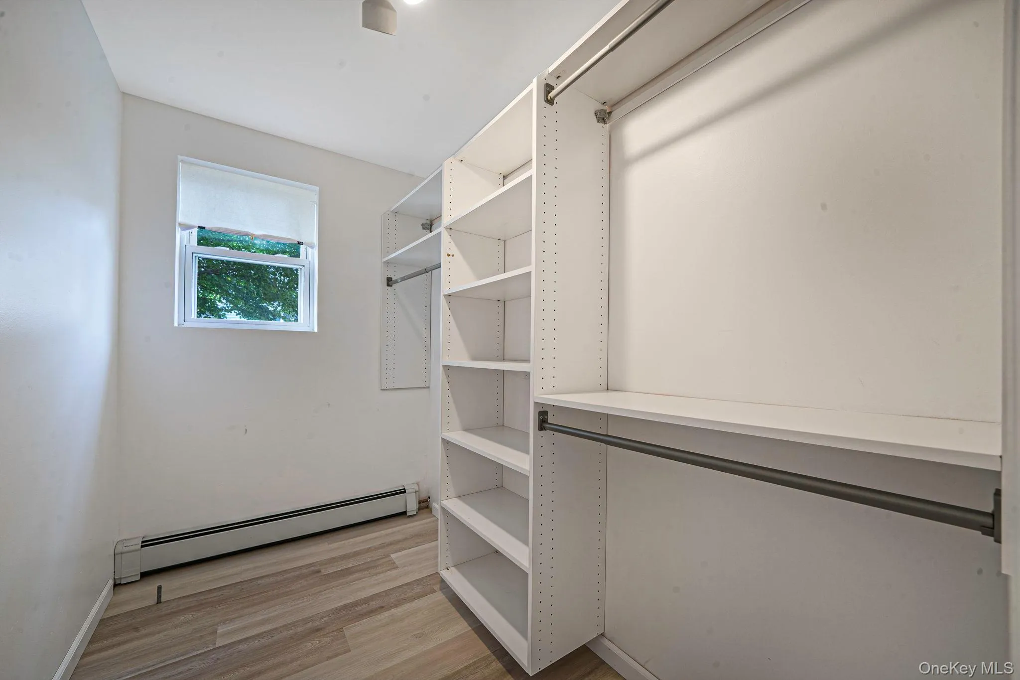 Walk in closet featuring a baseboard heating unit and light wood finished floors Walk in closet featuring a baseboard heating unit and light wood finished floors