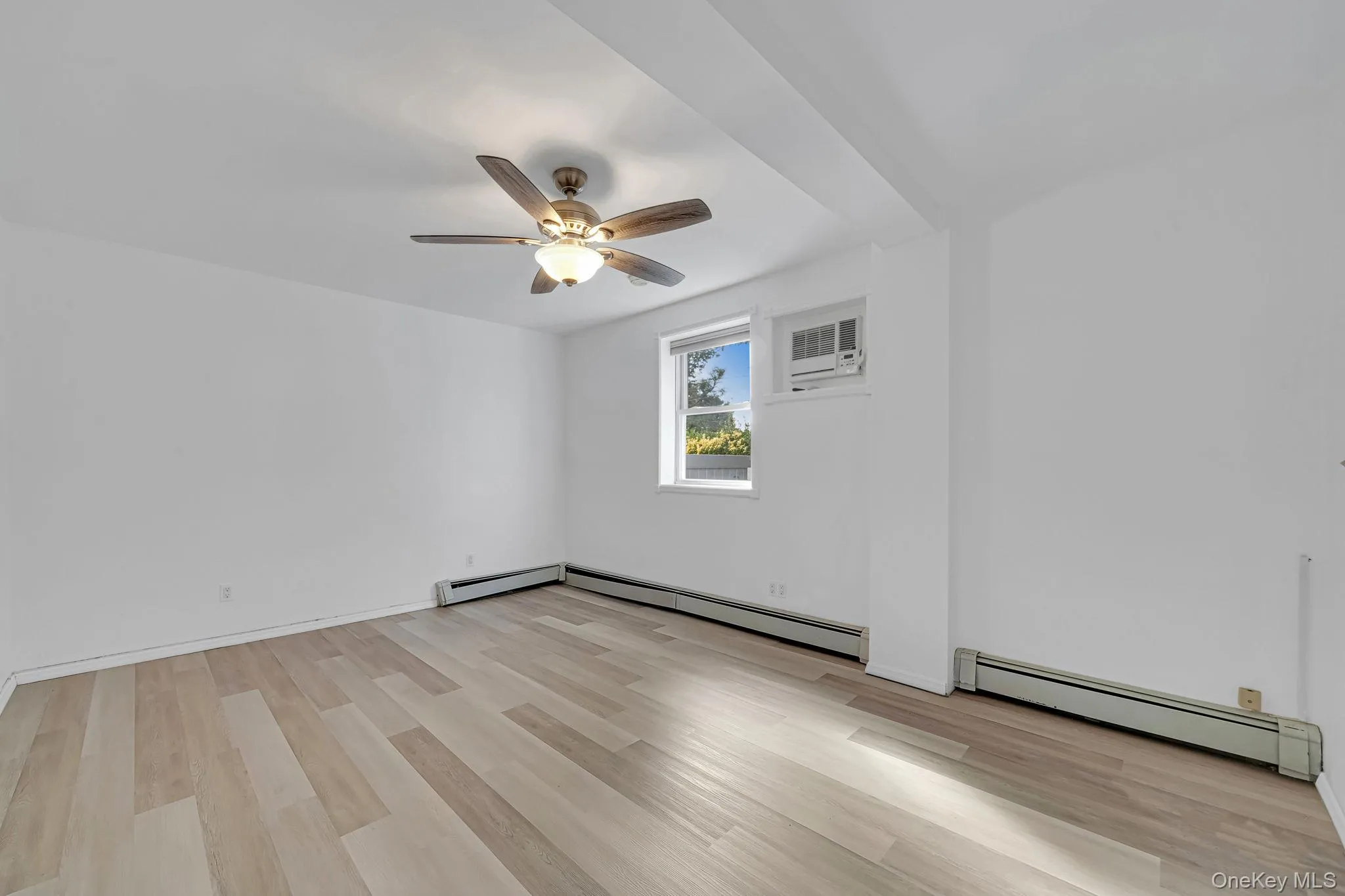 Unfurnished room featuring a baseboard radiator, light wood-style flooring, and a ceiling fan Unfurnished room featuring a baseboard radiator, light wood-style flooring, and a ceiling fan