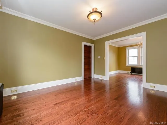 Empty room with crown molding, a chandelier, dark wood-type flooring, and radiator Empty room with crown molding, a chandelier, dark wood-type flooring, and radiator