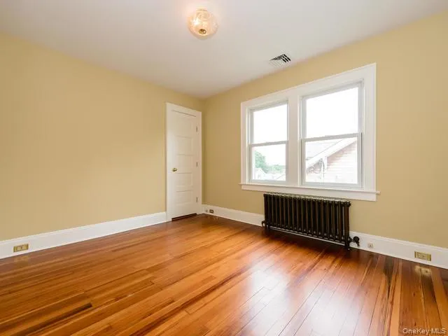 Unfurnished room featuring radiator and light wood-type flooring Unfurnished room featuring radiator and light wood-type flooring