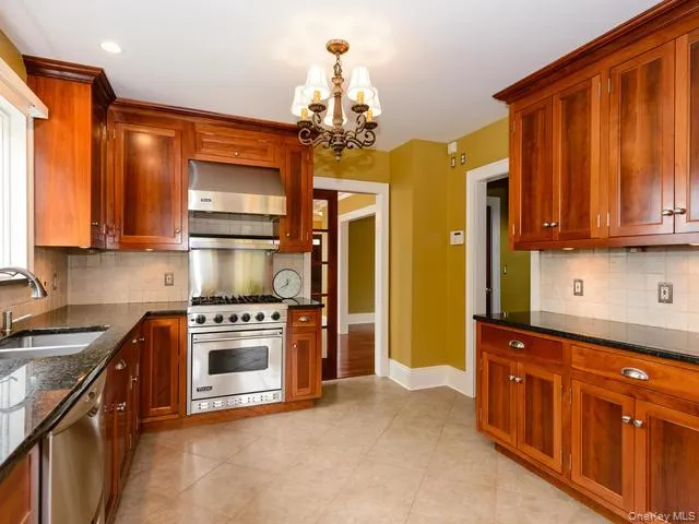 Kitchen with decorative backsplash, dark stone counters, appliances with stainless steel finishes, and wall chimney exhaust hood Kitchen with decorative backsplash, dark stone counters, appliances with stainless steel finishes, and wall chimney exhaust hood