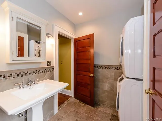 Half bathroom with tile walls, stacked washer / dryer, a wainscoted wall, and light tile patterned floors Half bathroom with tile walls, stacked washer / dryer, a wainscoted wall, and light tile patterned floors