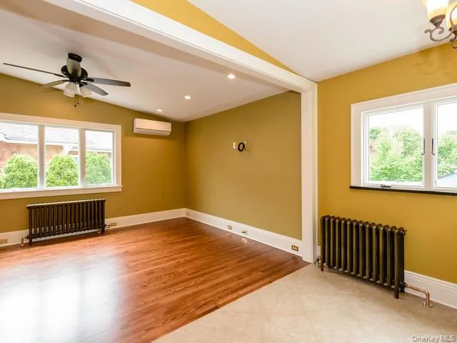Unfurnished room featuring radiator, light wood-type flooring, vaulted ceiling, a wall mounted AC, and recessed lighting Unfurnished room featuring radiator, light wood-type flooring, vaulted ceiling, a wall mounted AC, and recessed lighting