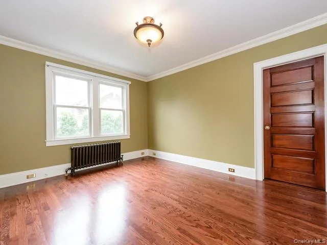 Spare room with radiator, ornamental molding, and wood finished floors Spare room with radiator, ornamental molding, and wood finished floors