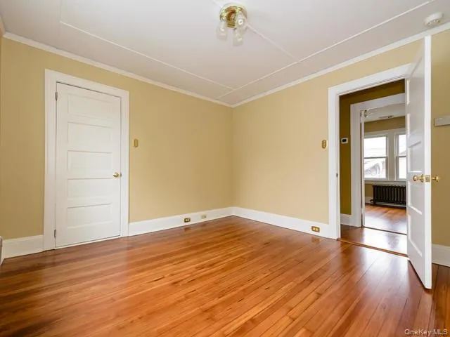 Spare room featuring light wood-style flooring, radiator, and ornamental molding Spare room featuring light wood-style flooring, radiator, and ornamental molding