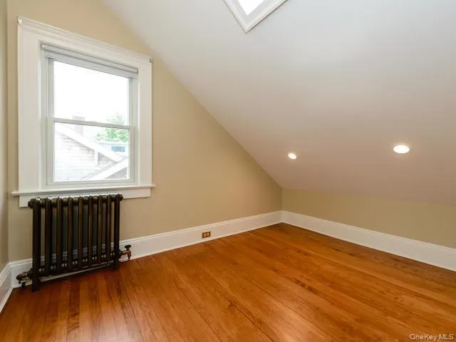 Additional living space featuring radiator heating unit, lofted ceiling, a skylight, and light wood-type flooring Additional living space featuring radiator heating unit, lofted ceiling, a skylight, and light wood-type flooring