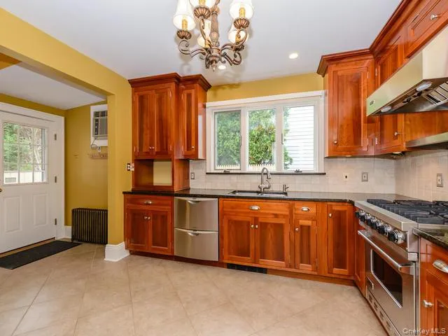 Kitchen with appliances with stainless steel finishes, a chandelier, under cabinet range hood, radiator, and dark stone countertops Kitchen with appliances with stainless steel finishes, a chandelier, under cabinet range hood, radiator, and dark stone countertops