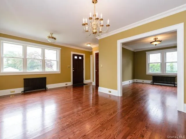 Unfurnished living room featuring radiator, ornamental molding, wood finished floors, and a chandelier Unfurnished living room featuring radiator, ornamental molding, wood finished floors, and a chandelier