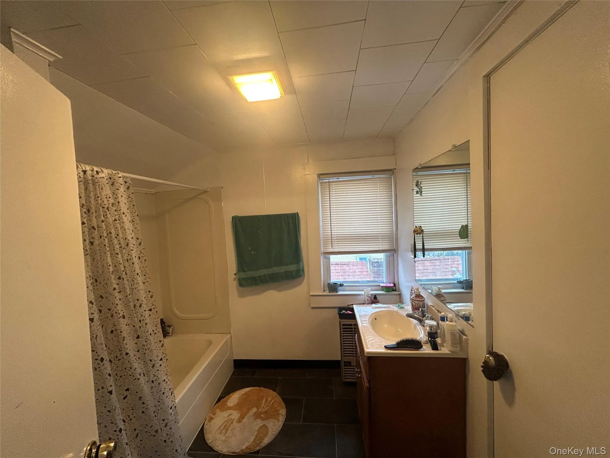 Bathroom with vanity, dark tile patterned floors, shower / bath combo with shower curtain, and vaulted ceiling Bathroom with vanity, dark tile patterned floors, shower / bath combo with shower curtain, and vaulted ceiling