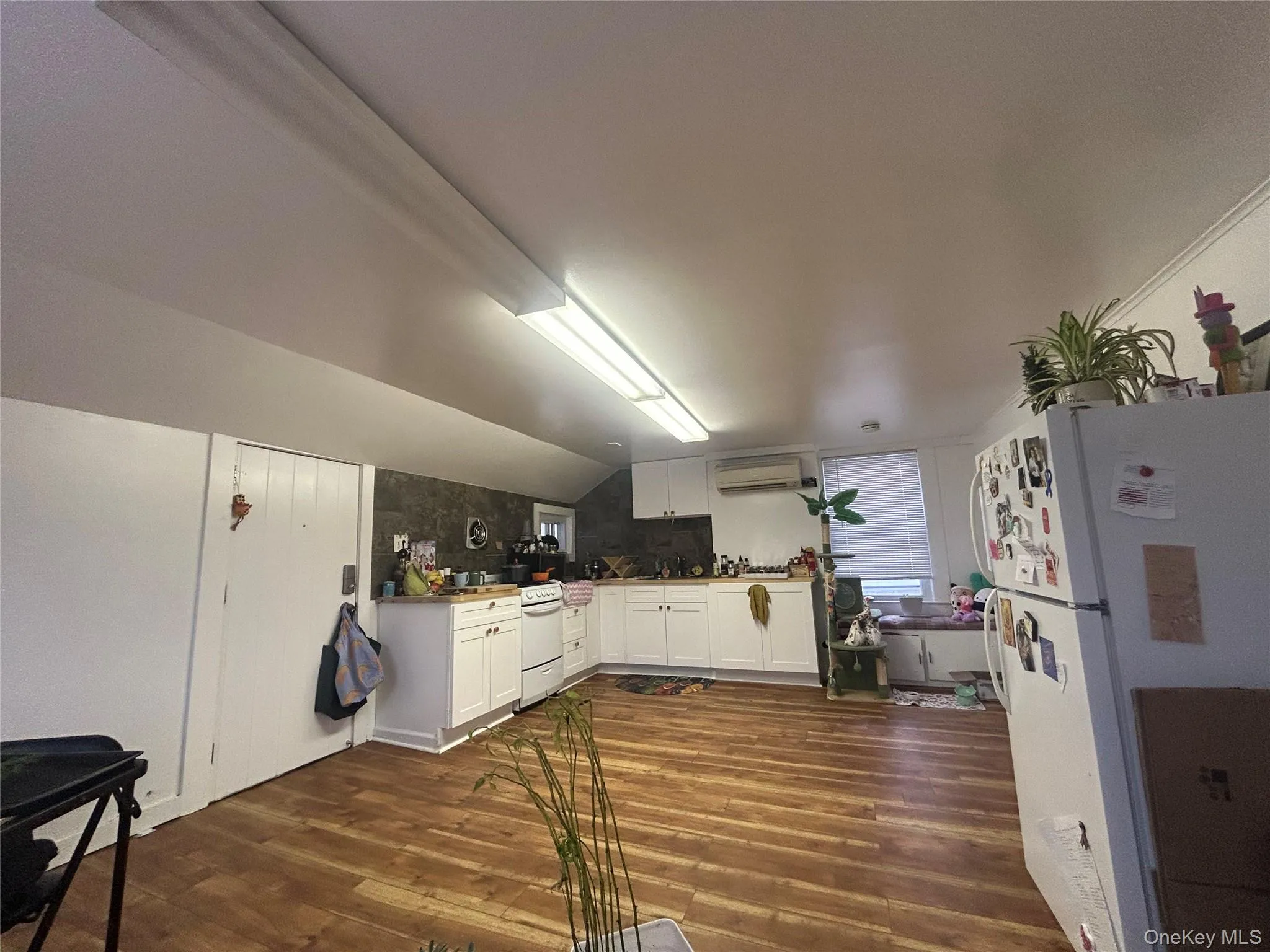 Kitchen with white cabinetry, white appliances, dark wood-style floors, vaulted ceiling, and a wall unit AC Kitchen with white cabinetry, white appliances, dark wood-style floors, vaulted ceiling, and a wall unit AC