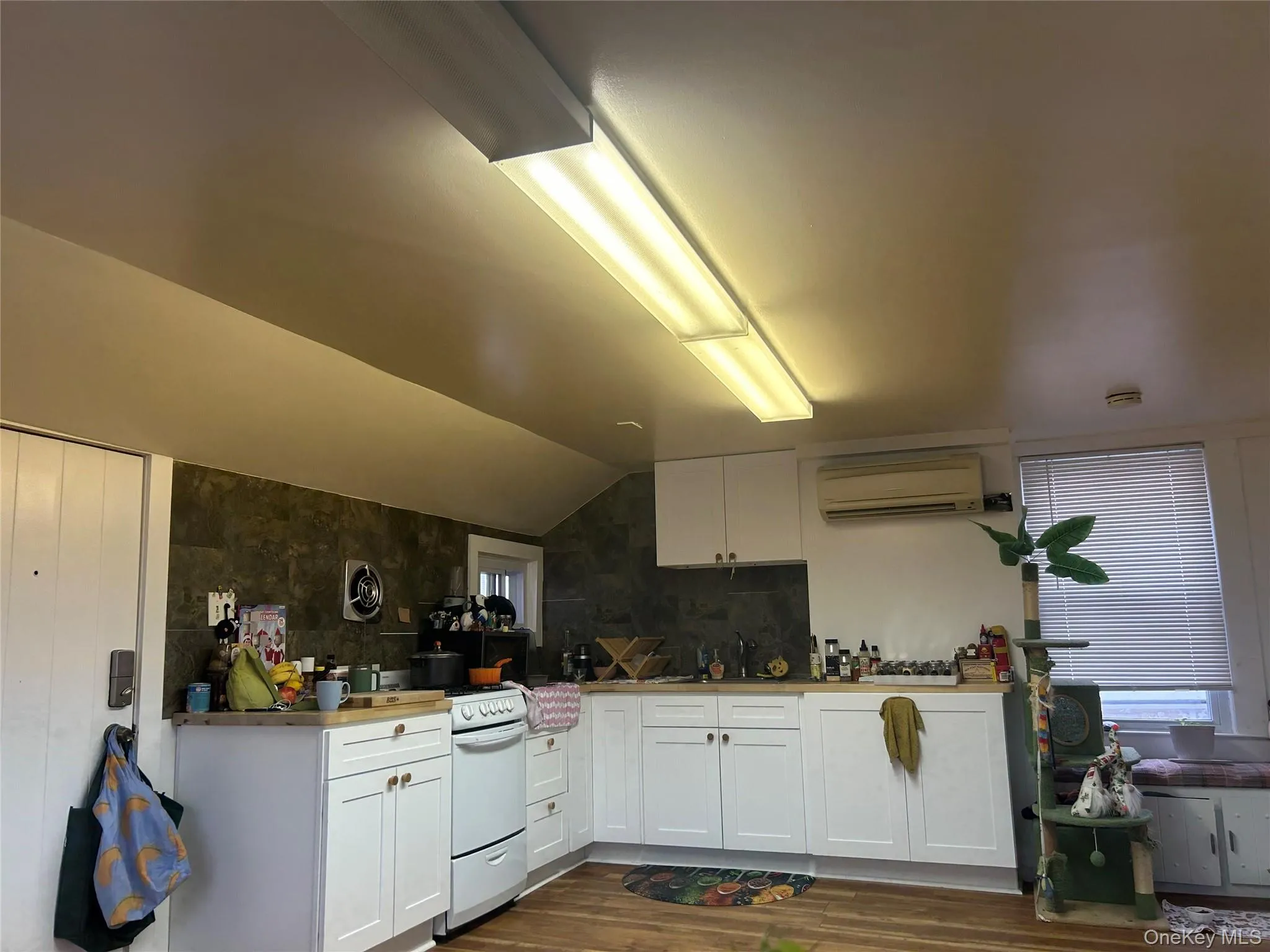 Kitchen featuring white cabinetry, white range with gas cooktop, lofted ceiling, dark wood-type flooring, and a wall mounted AC Kitchen featuring white cabinetry, white range with gas cooktop, lofted ceiling, dark wood-type flooring, and a wall mounted AC