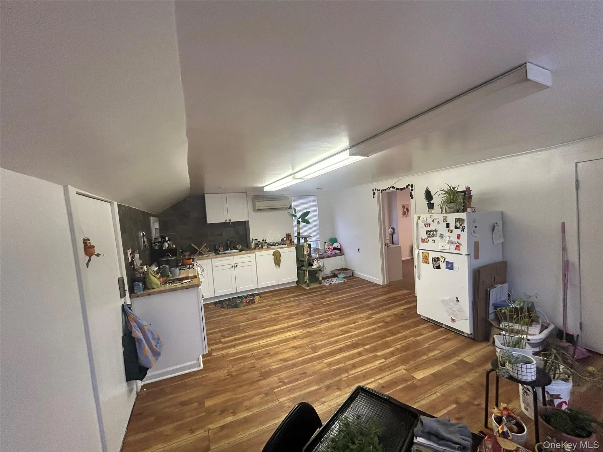 Kitchen with white cabinets, freestanding refrigerator, dark wood-type flooring, lofted ceiling, and a wall mounted air conditioner Kitchen with white cabinets, freestanding refrigerator, dark wood-type flooring, lofted ceiling, and a wall mounted air conditioner