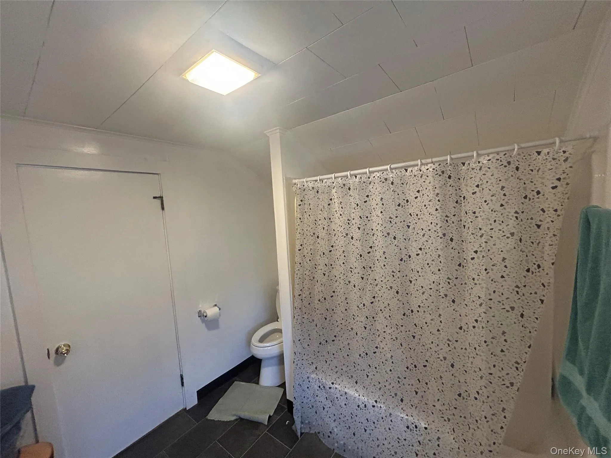 Bathroom with dark tile patterned flooring, shower / bath combination with curtain, and lofted ceiling Bathroom with dark tile patterned flooring, shower / bath combination with curtain, and lofted ceiling