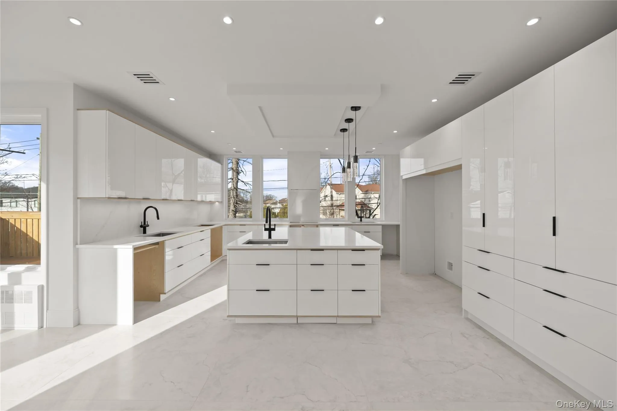 Kitchen with modern cabinets, white cabinetry, decorative light fixtures, light marble finish floors, and light stone countertops Kitchen with modern cabinets, white cabinetry, decorative light fixtures, light marble finish floors, and light stone countertops