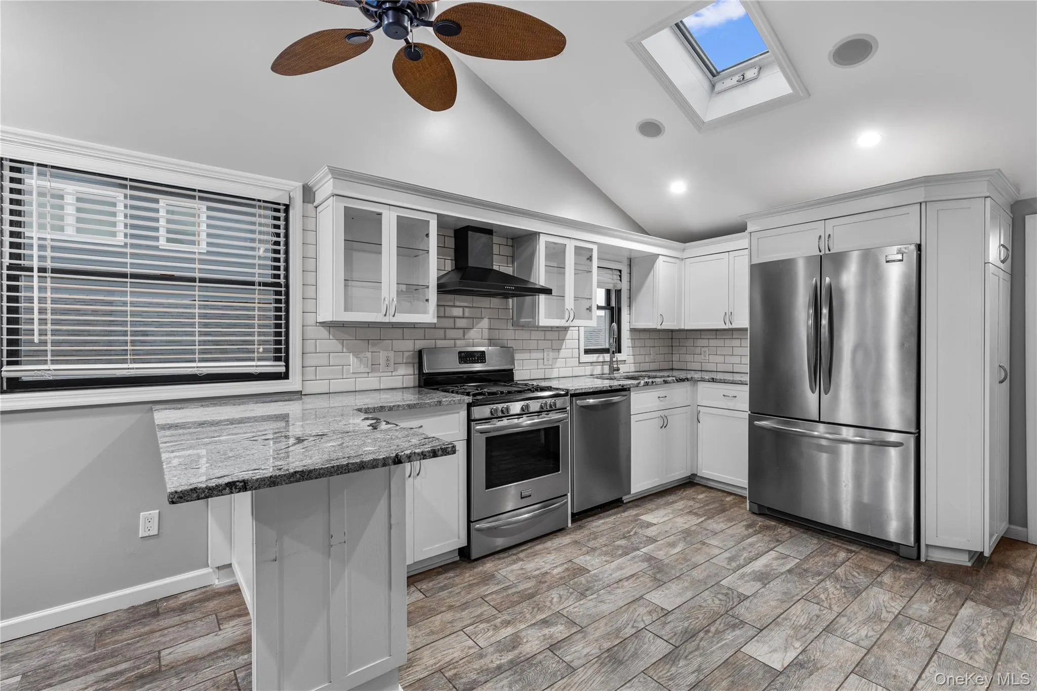 Kitchen with stainless steel appliances, dark stone counters, white cabinets, glass insert cabinets, and high vaulted ceiling Kitchen with stainless steel appliances, dark stone counters, white cabinets, glass insert cabinets, and high vaulted ceiling