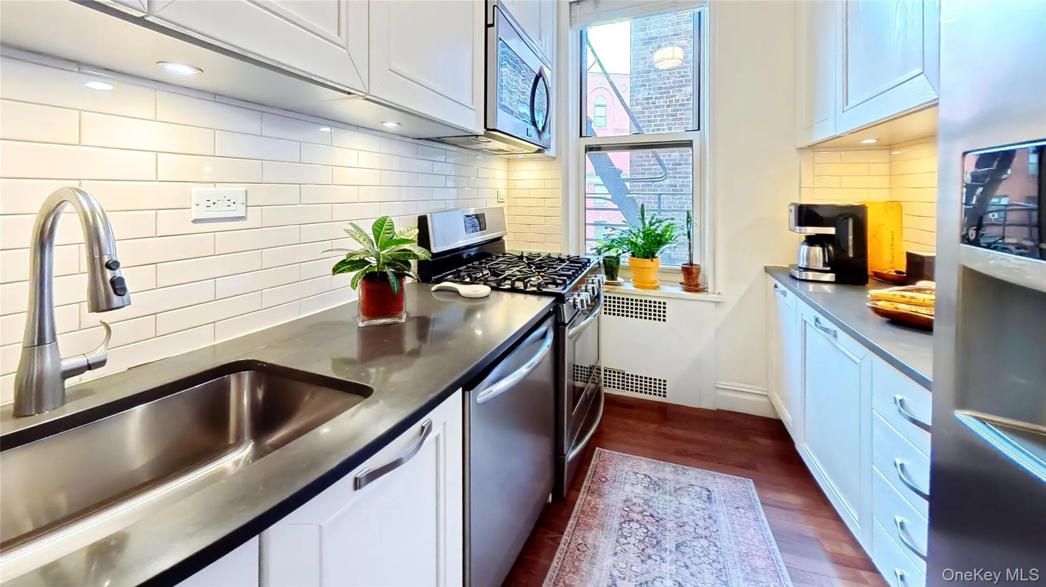 Kitchen featuring white cabinets, appliances with stainless steel finishes, backsplash, and dark wood-style flooring Kitchen featuring white cabinets, appliances with stainless steel finishes, backsplash, and dark wood-style flooring