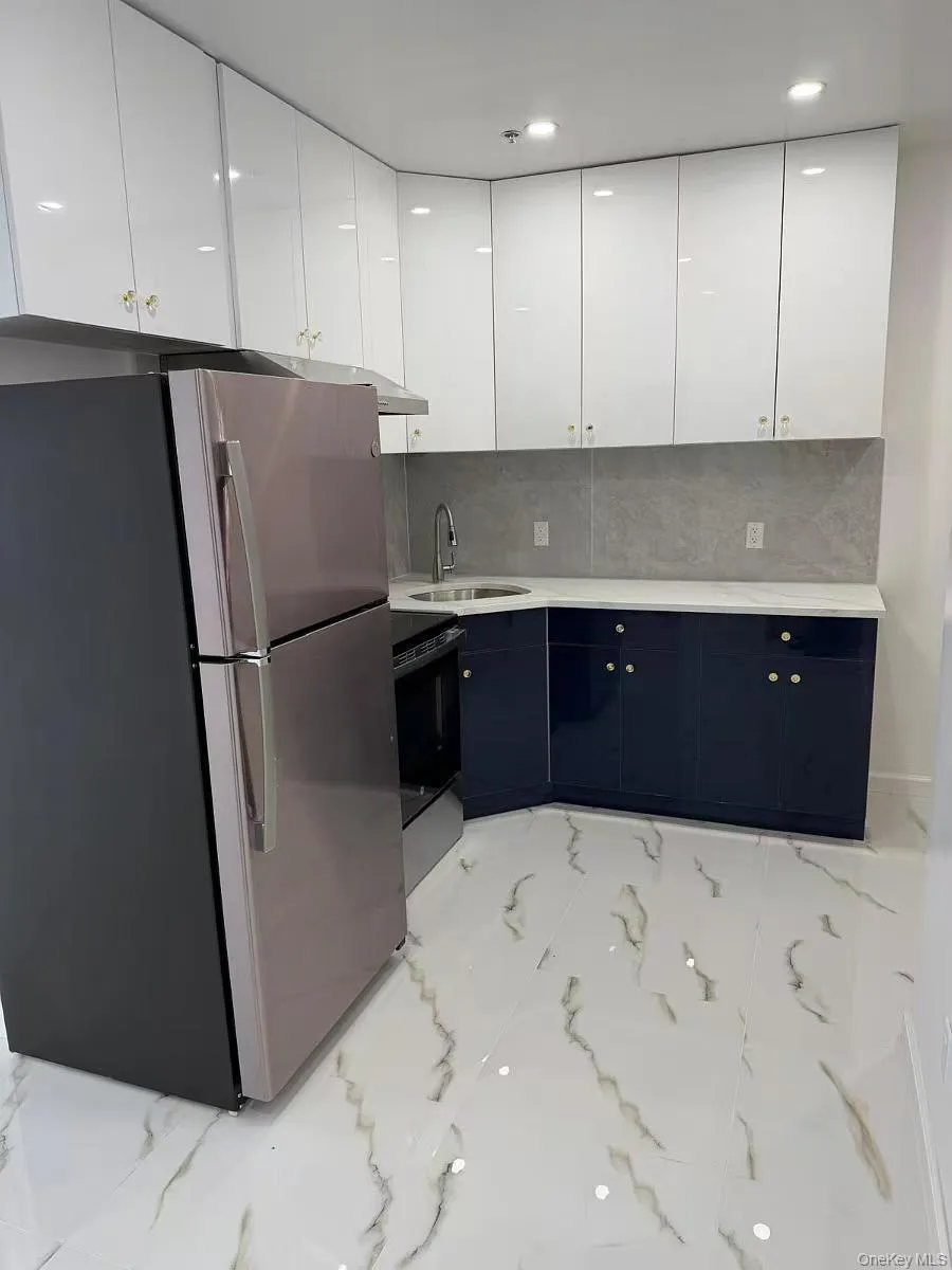 Kitchen with white cabinets, freestanding refrigerator, light marble finish floors, black range with electric stovetop, and tasteful backsplash Kitchen with white cabinets, freestanding refrigerator, light marble finish floors, black range with electric stovetop, and tasteful backsplash