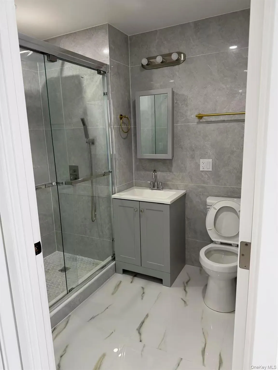Full bath with vanity, a shower stall, tile walls, and light marble finish floors Full bath with vanity, a shower stall, tile walls, and light marble finish floors