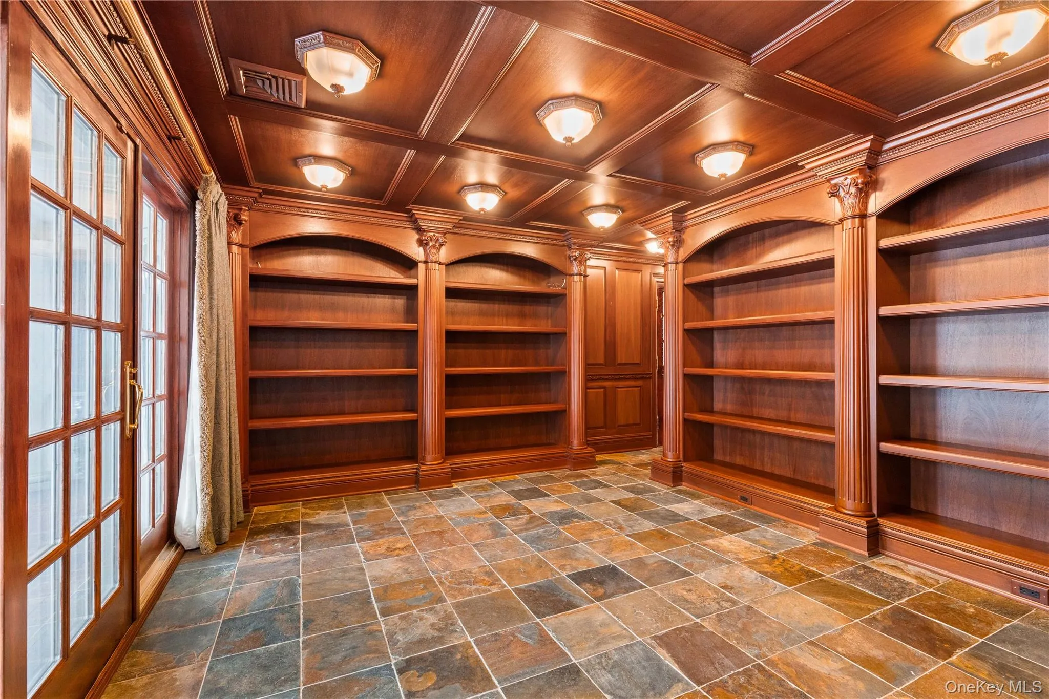 Mahogany library crowned with custom built-ins, an intimate wood coffered ceiling with illuminated lighting, ornamental moldings, and dark stone finish floors -French doors out to deck & a side exit Mahogany library crowned with custom built-ins, an intimate wood coffered ceiling with illuminated lighting, ornamental moldings, and dark stone finish floors -French doors out to deck & a side exit