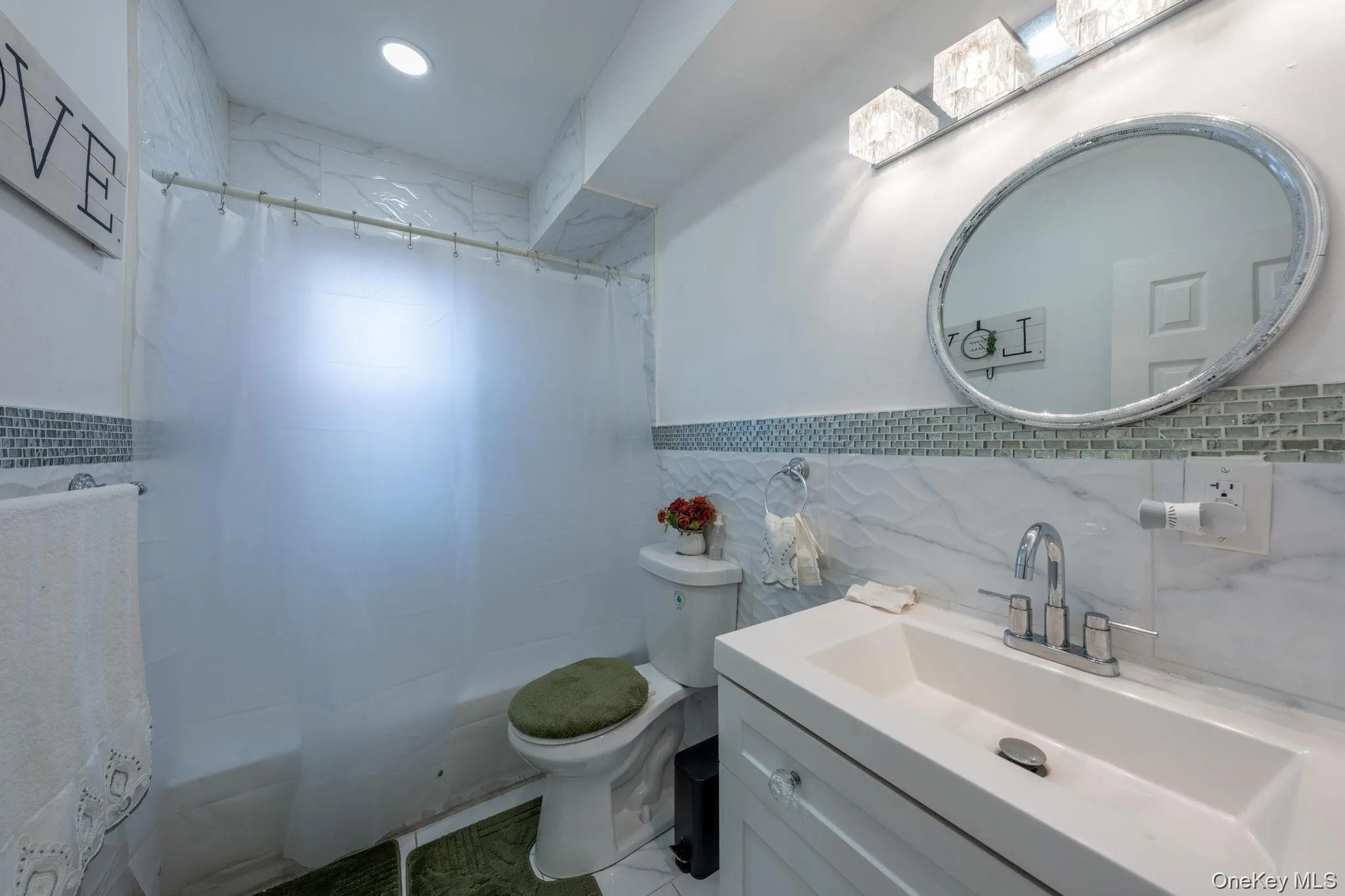 Full bathroom featuring tile walls, vanity, shower / bath combo, and a wainscoted wall Full bathroom featuring tile walls, vanity, shower / bath combo, and a wainscoted wall