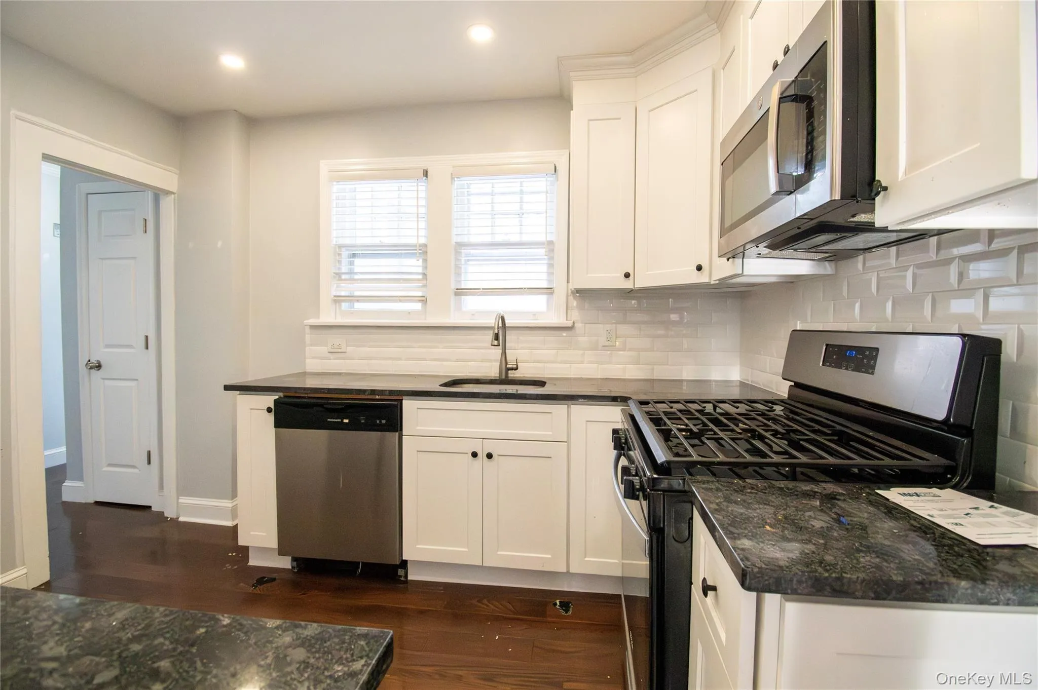 Kitchen featuring stainless steel appliances, white cabinets, dark stone countertops, dark wood-style flooring, and decorative backsplash Kitchen featuring stainless steel appliances, white cabinets, dark stone countertops, dark wood-style flooring, and decorative backsplash