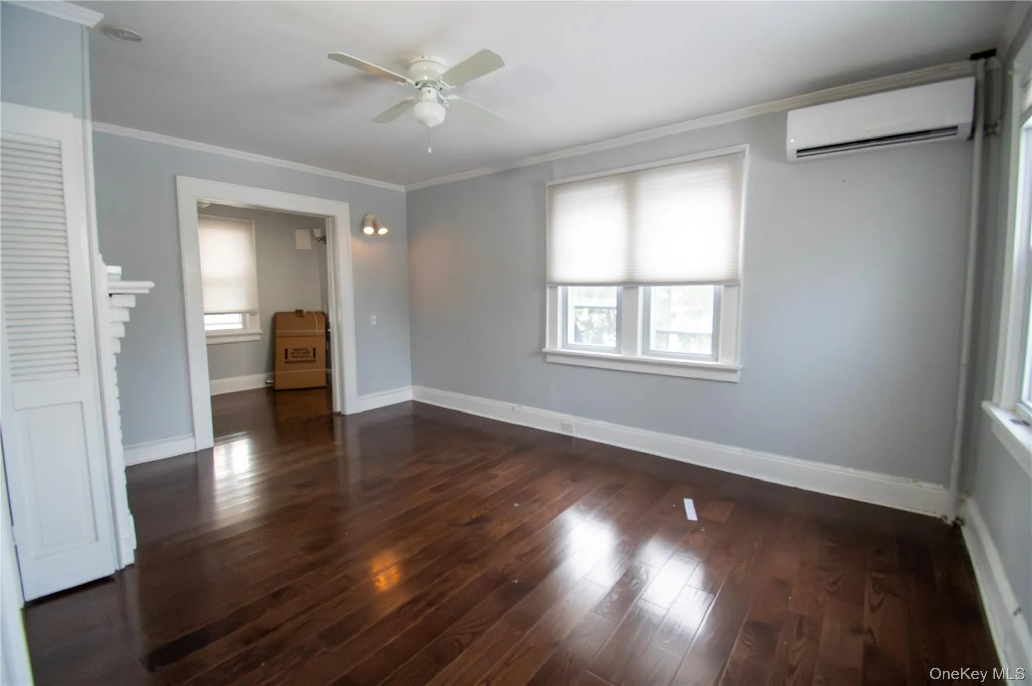 Unfurnished bedroom with ornamental molding, an AC wall unit, ceiling fan, and dark wood-style flooring Unfurnished bedroom with ornamental molding, an AC wall unit, ceiling fan, and dark wood-style flooring