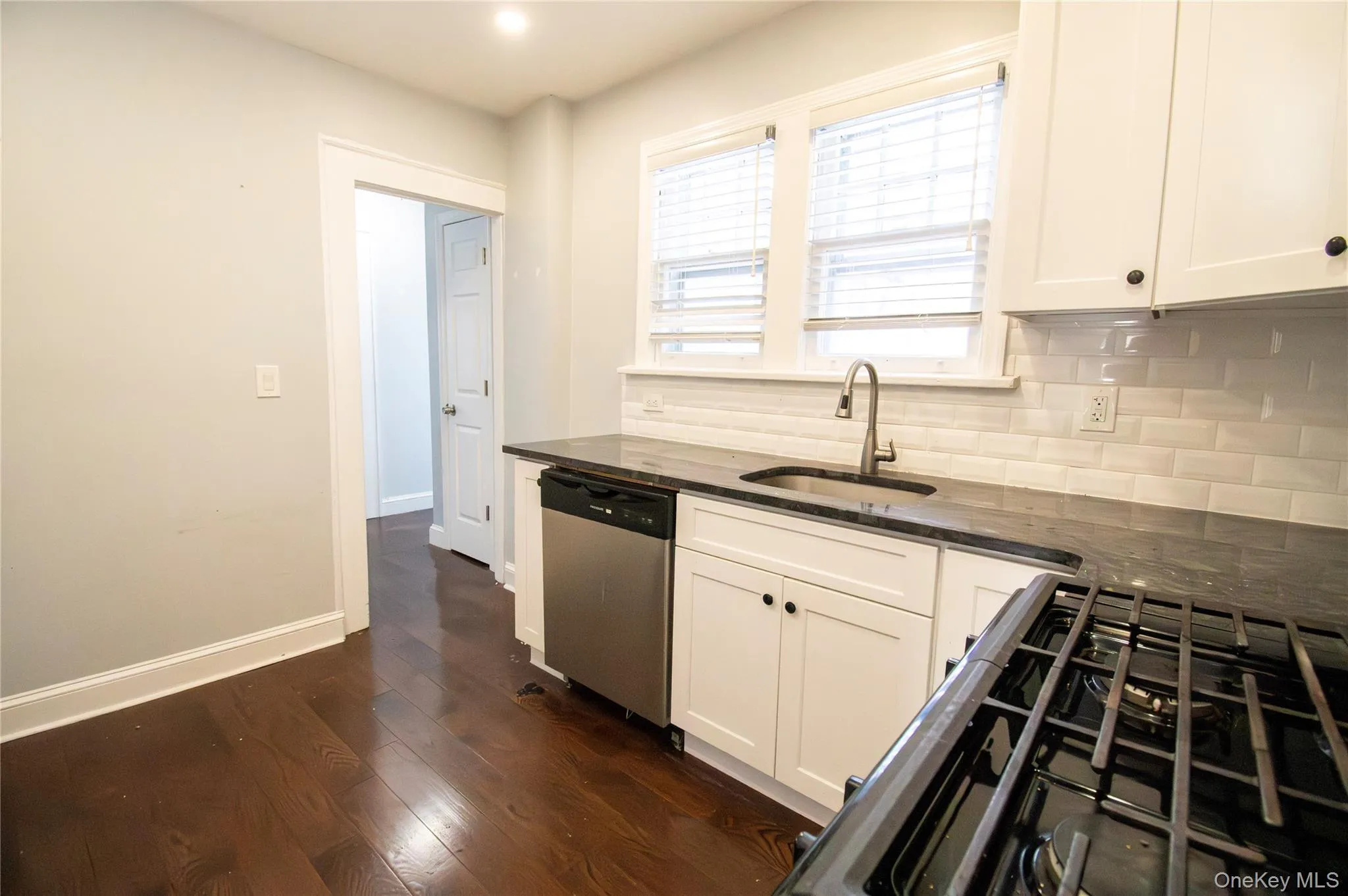 Kitchen featuring black gas stove, dark stone counters, stainless steel dishwasher, white cabinetry, and dark wood-style flooring Kitchen featuring black gas stove, dark stone counters, stainless steel dishwasher, white cabinetry, and dark wood-style flooring
