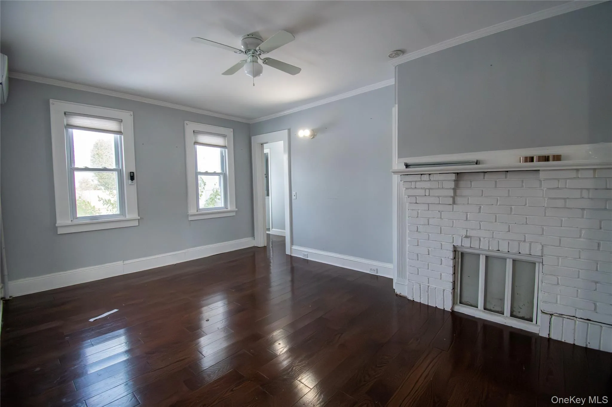 Unfurnished living room with ornamental molding, a brick fireplace, dark wood-style flooring, and a ceiling fan Unfurnished living room with ornamental molding, a brick fireplace, dark wood-style flooring, and a ceiling fan