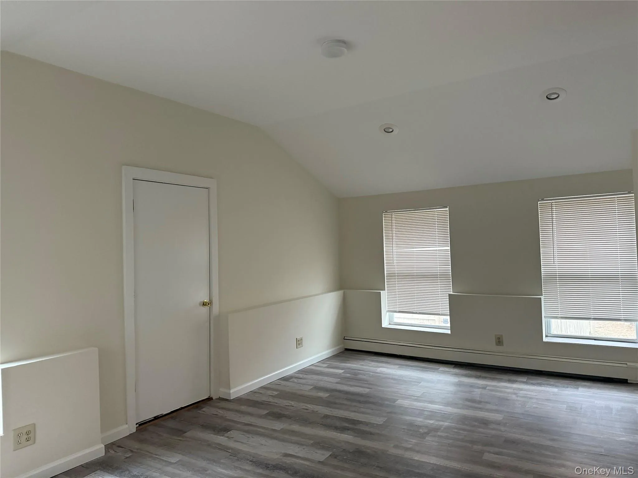 Empty room featuring a baseboard heating unit, lofted ceiling, and wood finished floors Empty room featuring a baseboard heating unit, lofted ceiling, and wood finished floors