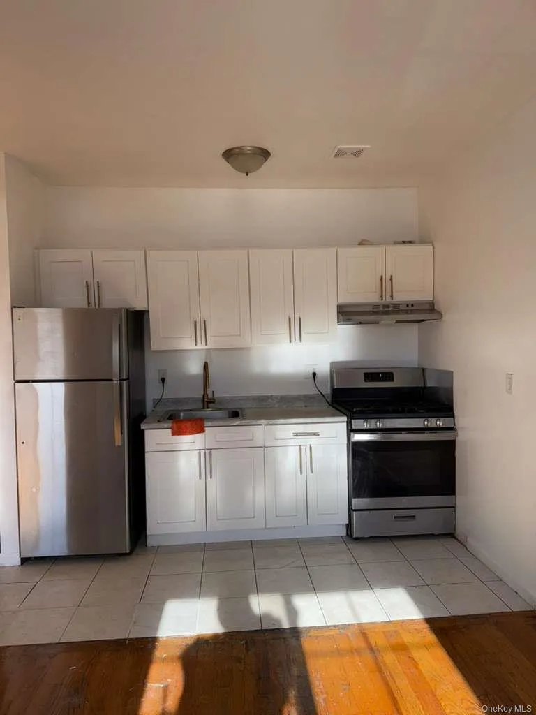Kitchen featuring appliances with stainless steel finishes, white cabinets, under cabinet range hood, and light wood finished floors Kitchen featuring appliances with stainless steel finishes, white cabinets, under cabinet range hood, and light wood finished floors