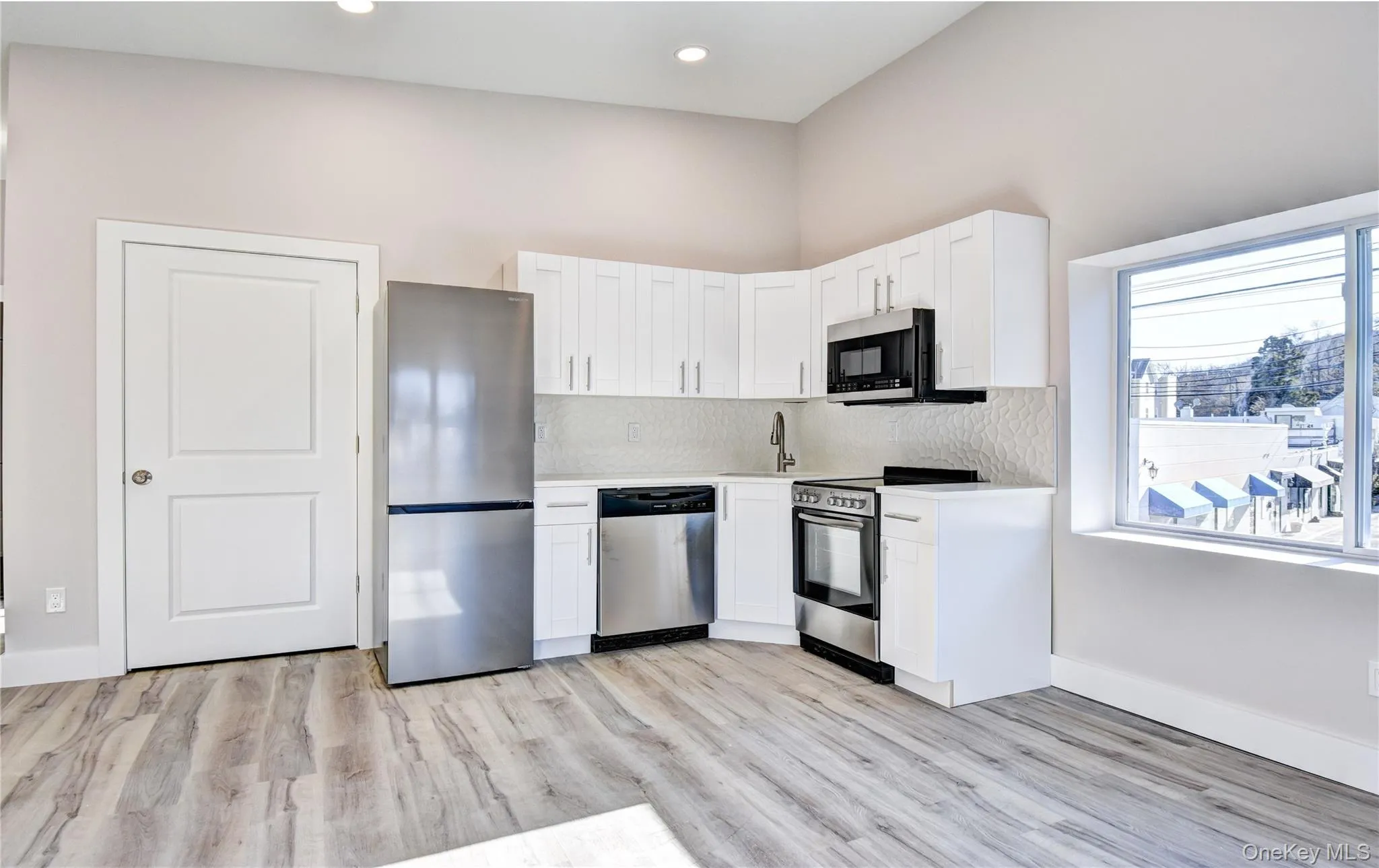 Kitchen with stainless steel appliances, white cabinetry, backsplash, light wood finished floors, and recessed lighting Kitchen with stainless steel appliances, white cabinetry, backsplash, light wood finished floors, and recessed lighting