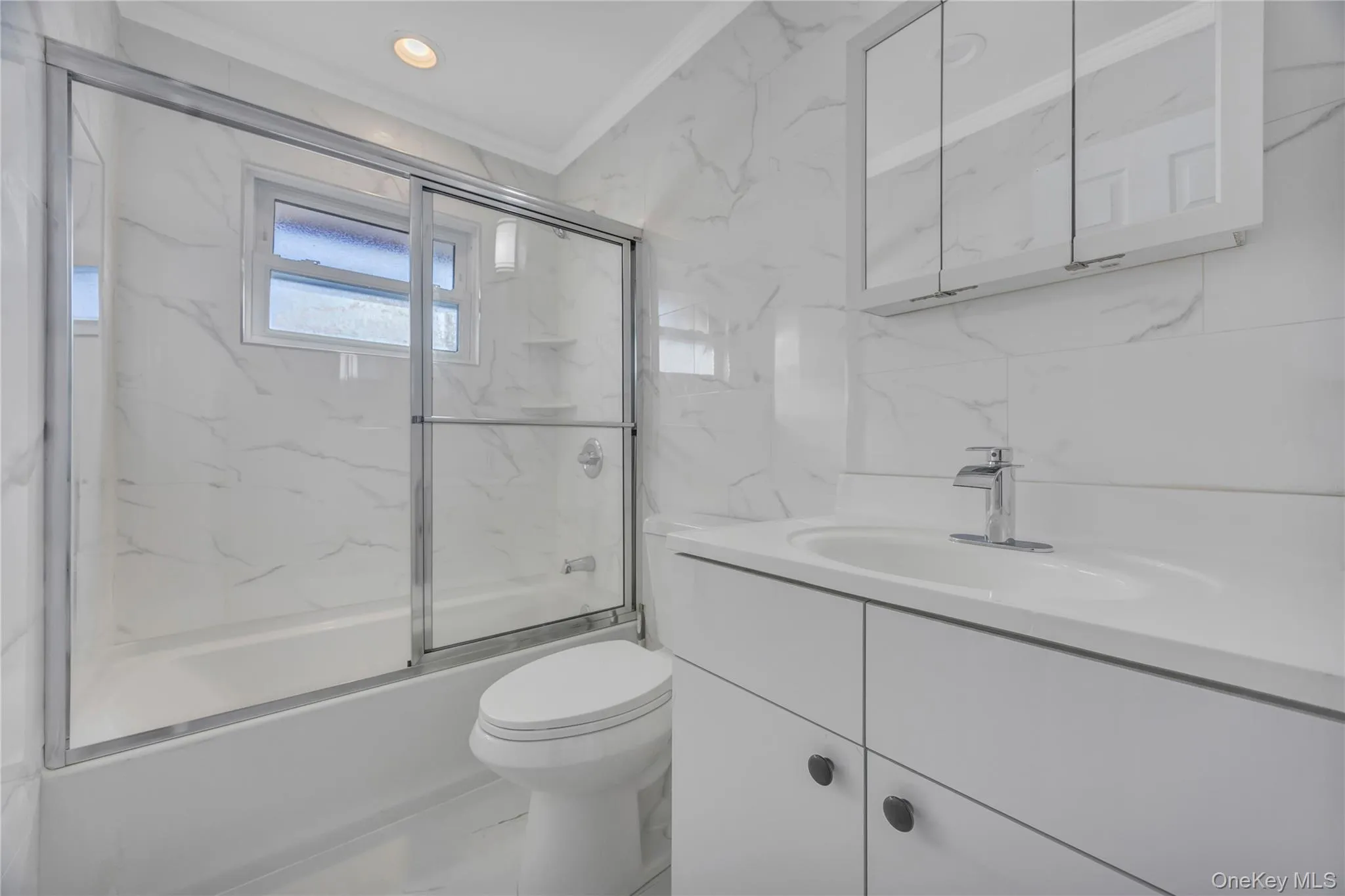 Bathroom featuring crown molding, vanity, shower / bath combination with glass door, marble tiled floors, and tile walls Bathroom featuring crown molding, vanity, shower / bath combination with glass door, marble tiled floors, and tile walls