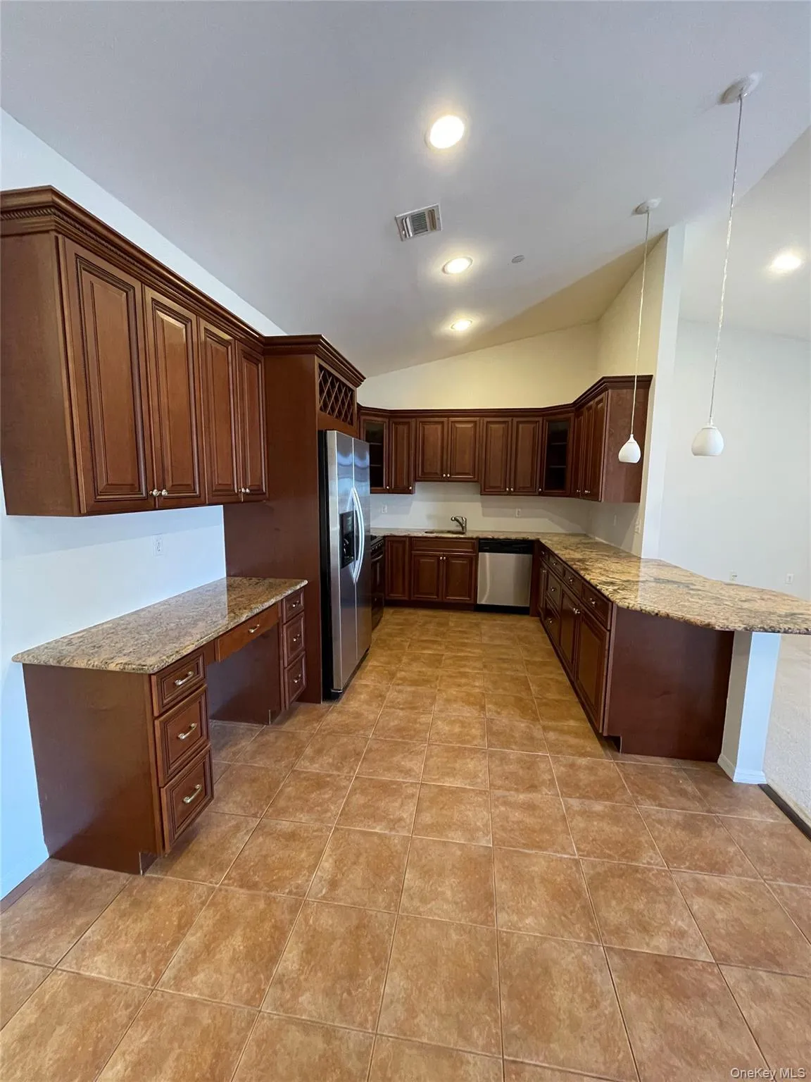 Kitchen with lofted ceiling, light stone counters, hanging light fixtures, stainless steel appliances, and a peninsula Kitchen with lofted ceiling, light stone counters, hanging light fixtures, stainless steel appliances, and a peninsula